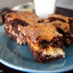 Three brownie squares on a plate next to a glass of milk