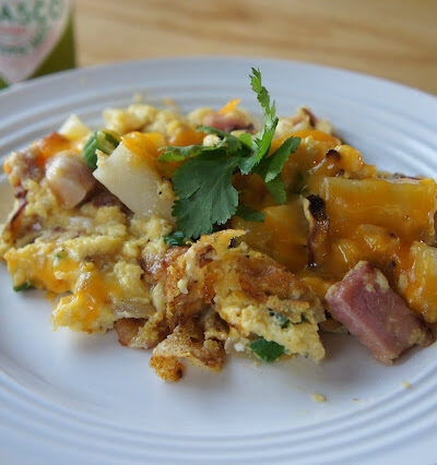 A plate displaying food; with ham, potatoes, eggs and cheese.