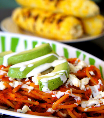 A bowl of red pasta with slices of avocado on top drizzled with a white sauce