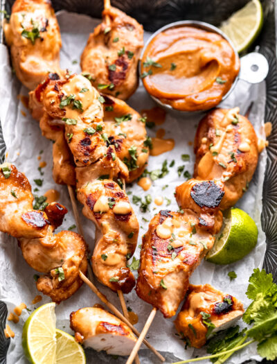 Cooked thai chicken satay on baking sheet with lime and peanut dipping sauce.