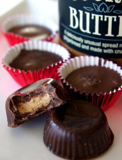 Chocolates on a table in front of a jar of cookie butter, one of the chocolate has a bite taken from it