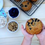 Two hands holding a Blueberry & Walnut Muffin above a table