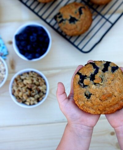 Two hands holding a Blueberry & Walnut Muffin above a table