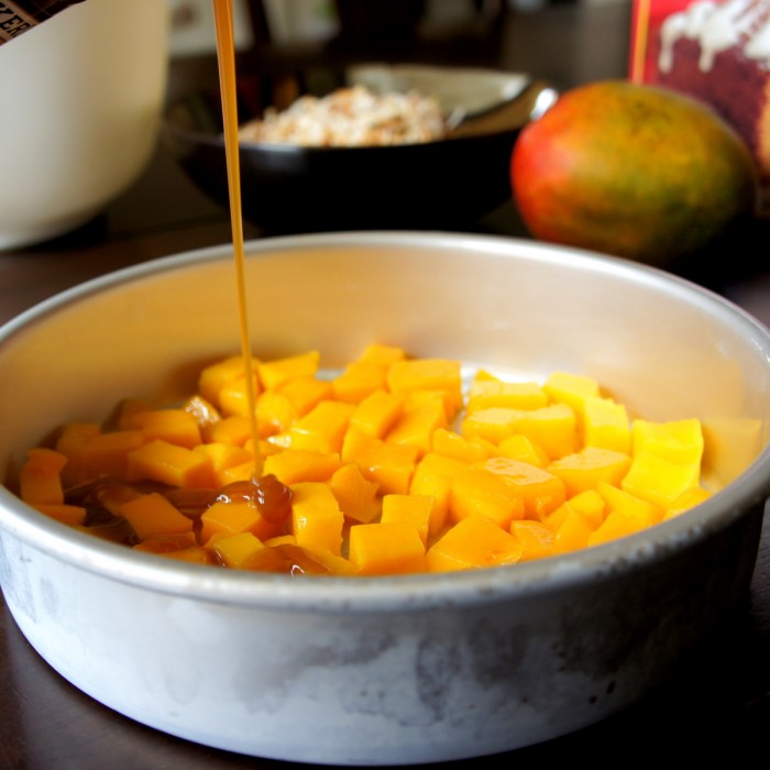 Cubed mangos in the bottom of a cake pan being drizzled with caramel sauce 