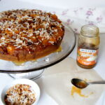 A cake on a cake platter topped caramel and coconut flakes