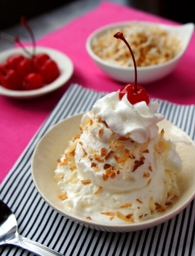 Two scoops of ice cream topped with whipped cream and a cherry in a bowl