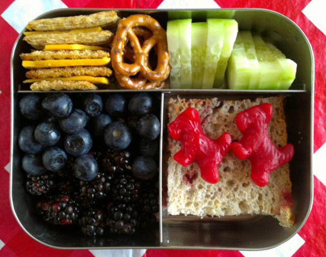 Bento lunch idea with crackers, pretzels, cucumber slices, blueberries, blackberries and bread