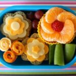 A bento lunch; sandwiches and fruit laid out to look like flowers