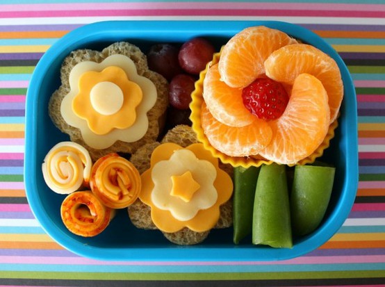 A bento lunch; sandwiches and fruit laid out to look like flowers