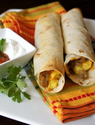 A close up of breakfast flautas displayed on a napkin, with sausage, egg and cheese in them