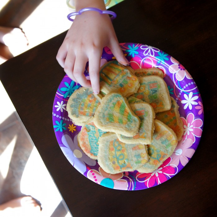 A hand taking a cookie from a plate of sugar cookies