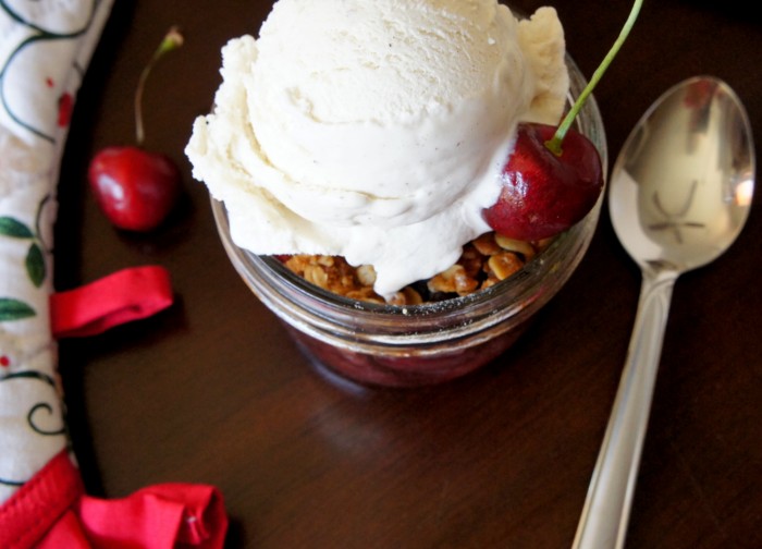 Sweet Cherry Crisp in a small mason jar topped with a scoop of vanilla ice-cream and a cherry 