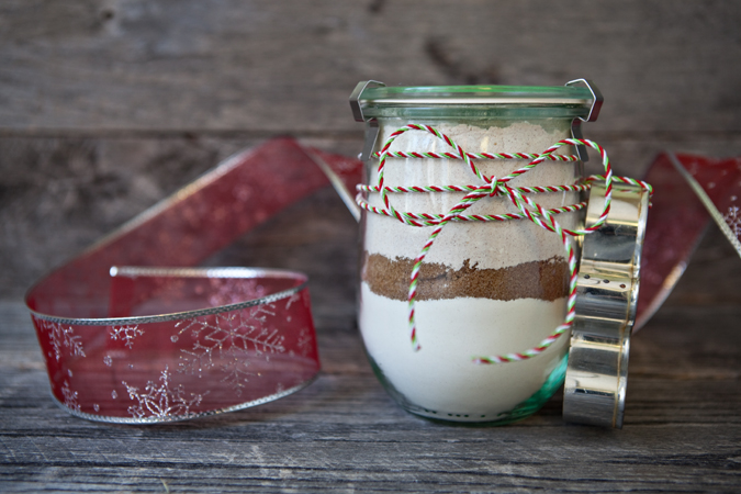 Gingerbread Cookie Mix in a a Jar displayed on a table next to some ribbon and a cookie cutter.