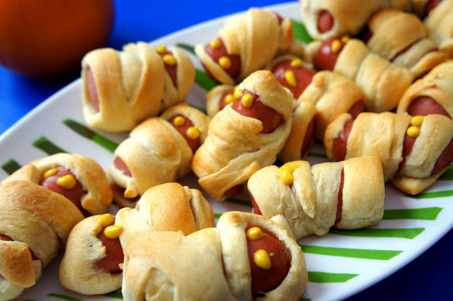 Mini Mummy Wrapped Hot Dogs on a plate with mustard eyeballs