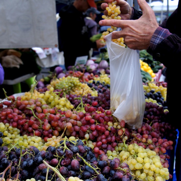 A large table of grapes and a man putting grapes in a plastic bag