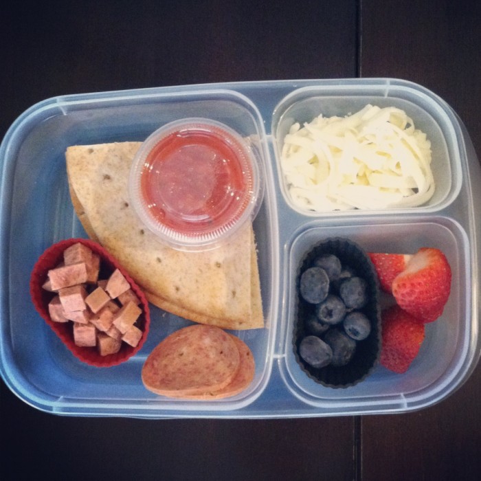 A plastic bento container filled with homemade lunch pizza makings and berries