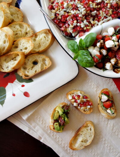 A close up of food on a table, with a tray of toasted baguette slices next to a tray of toppings and three Crostinis on a napkin