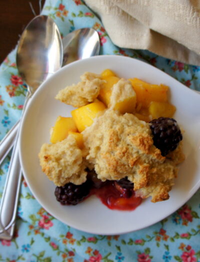 A plate with a scoop of cobbler on it with mango and blackberry