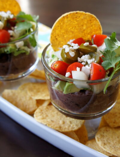 Five Layer Black Bean Dip in a glass cup over a tray of chips