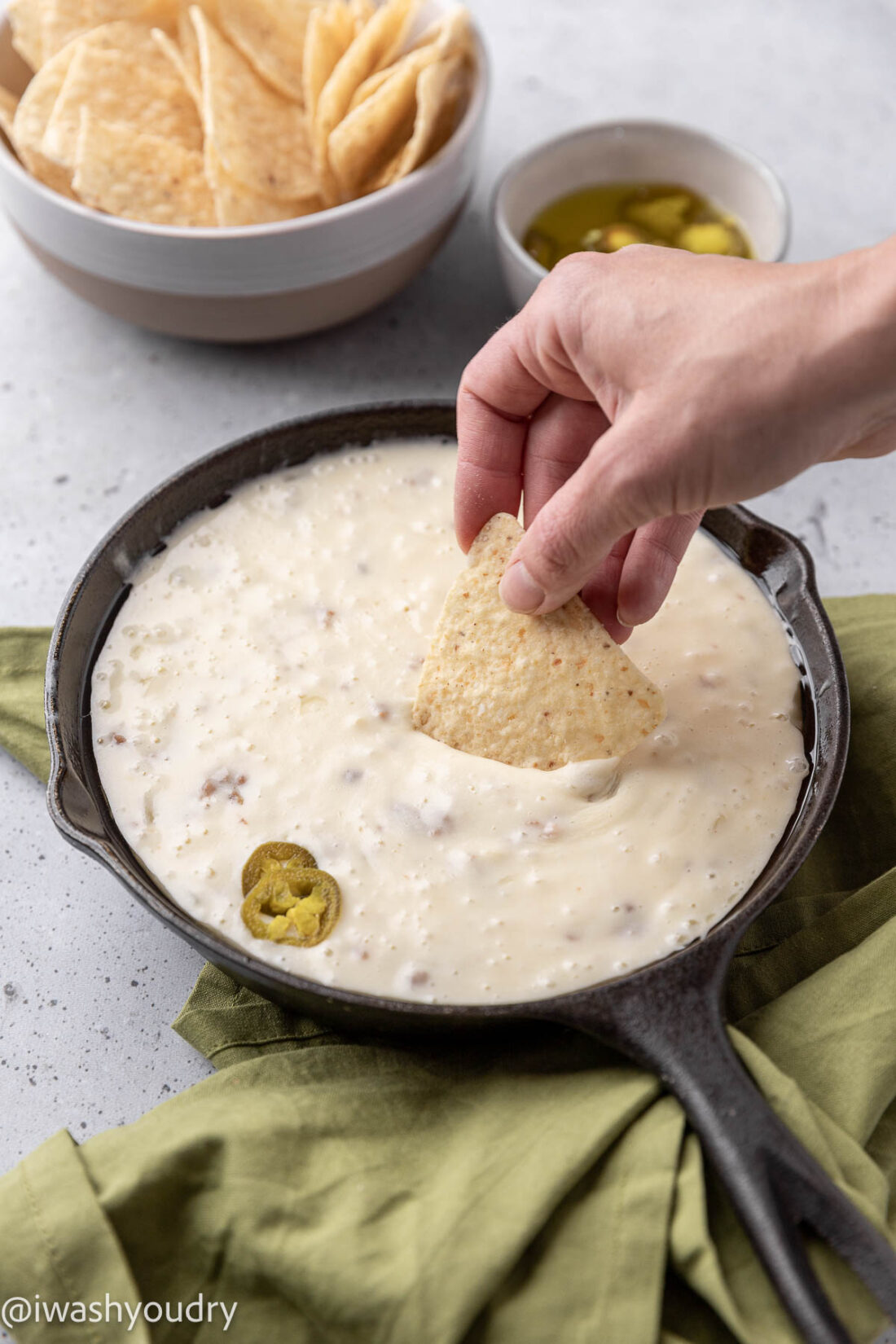 Chip dipping into warm queso fundido in black pan.