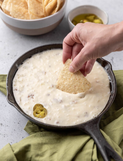 Chip dipping into warm queso fundido in black pan.