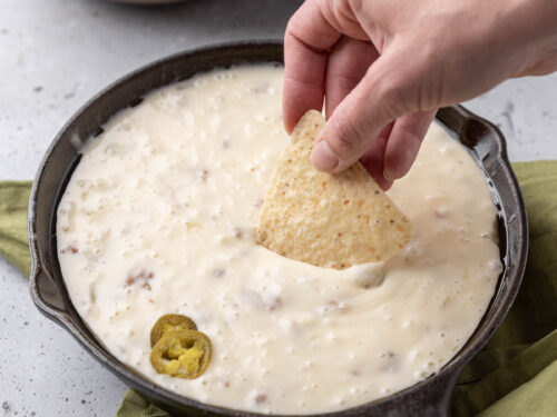 Chip dipping into warm queso fundido in black pan.