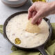 Chip dipping into warm queso fundido in black pan.