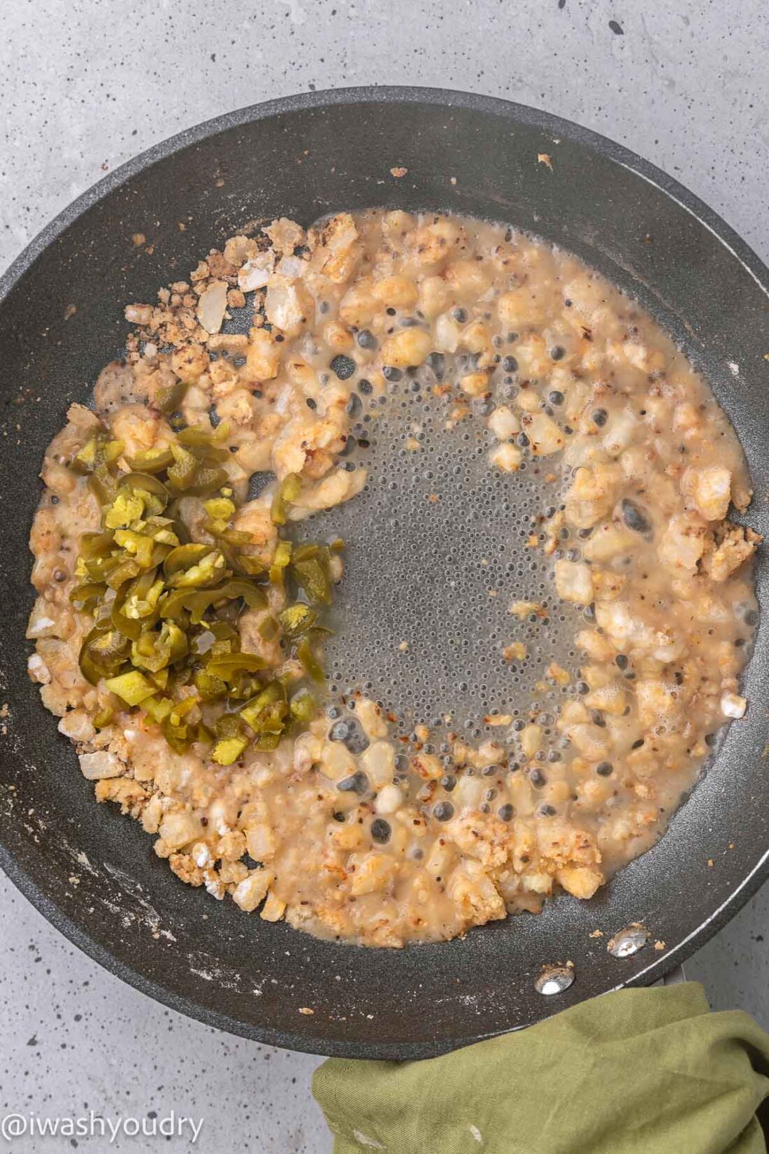 Jalapenos, onion, and cooking wine in black frying pan. 