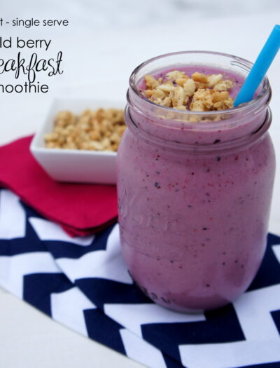 A smoothie in a glass cup with granola on top and a blue straw next to a small bowl of granola