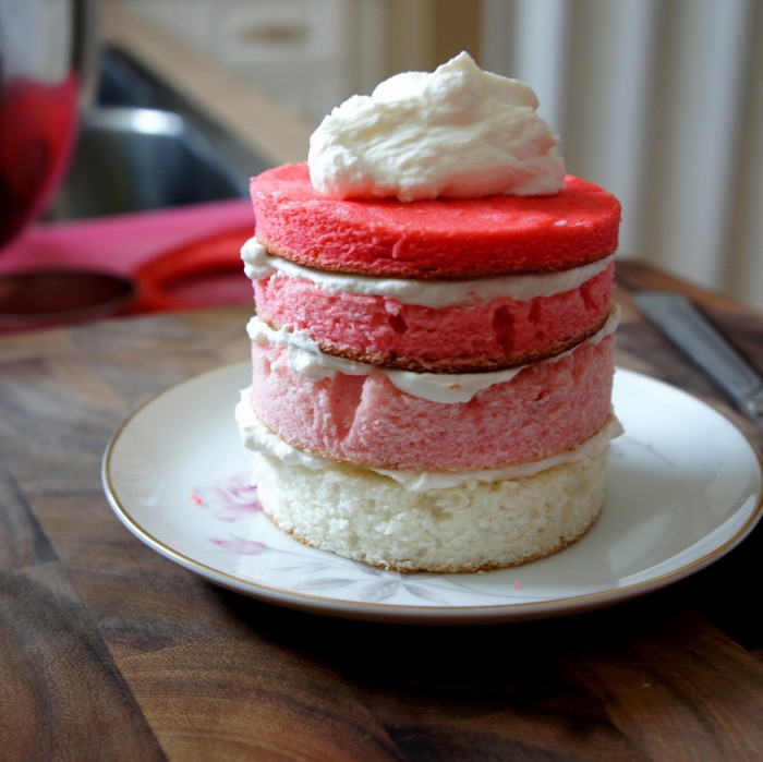 Four layers of cake pre-frosted on a plate with a pile of frosting on the top