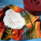 A pile of homemade tortillas in a colorful cloth next to a tortilla warmer