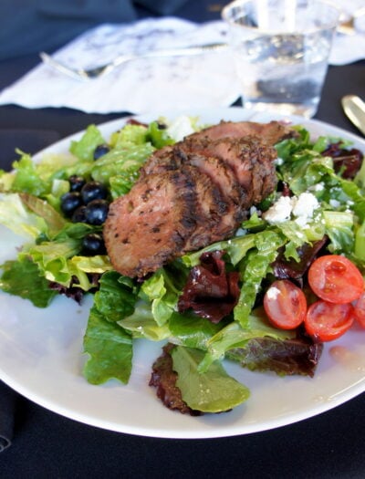 A plate with a white plate with sliced beef on a bed of lettuce and veggies