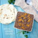 A square bowl of refried beans topped with cheese next to a small pile of tortillas