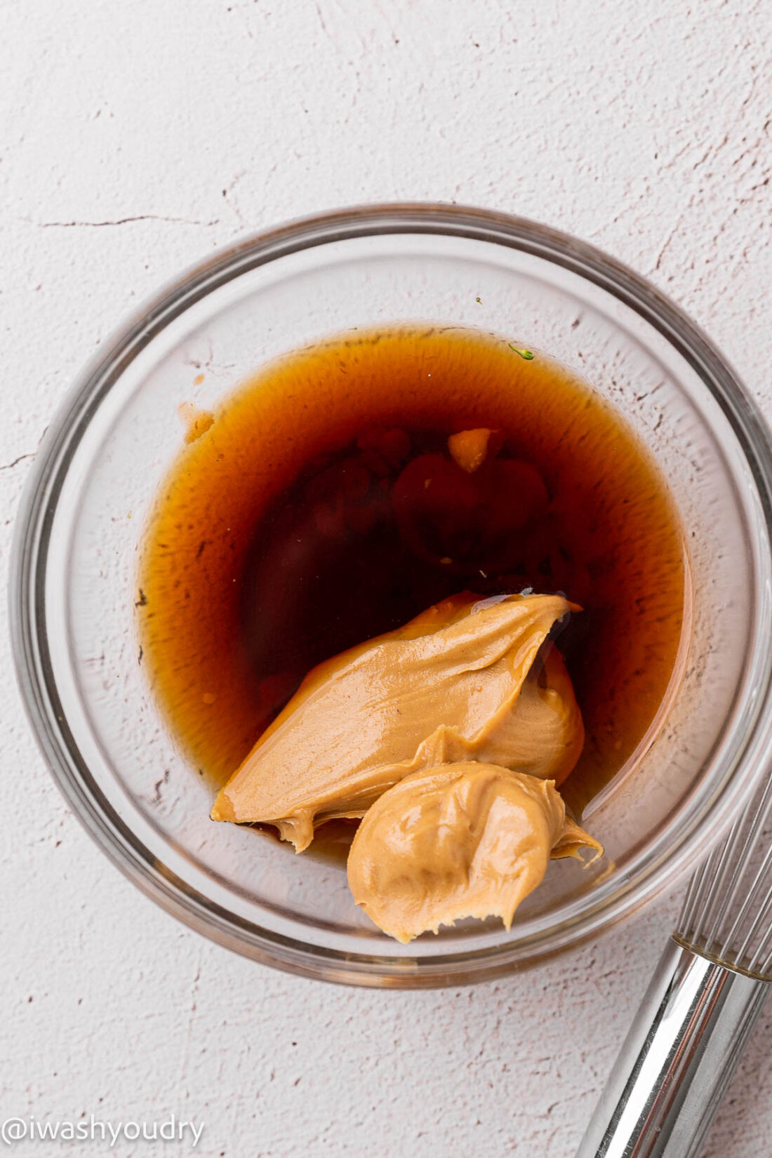 peanut sauce ingredients in clear bowl with soy sauce and sriracha.