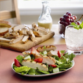 A salad on a plate topped with chicken and strawberry slices and a cutting board of chicken strips in the background