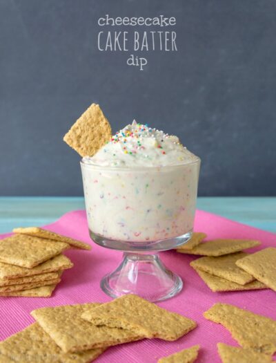 A desert cup filled with a dip and a graham cracker dipped in it titled, "Cheesecake Cake Batter Dip"