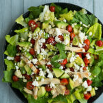 A close up of a salad topped with avocado chunks, veggies and cheese