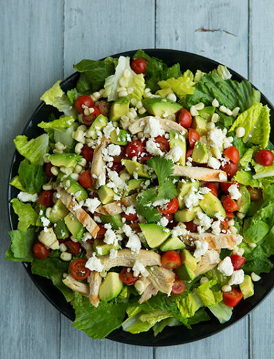 A close up of a salad topped with avocado chunks, veggies and cheese