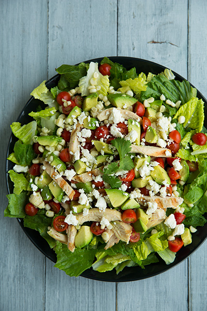 A close up of a salad topped with avocado chunks, veggies and cheese