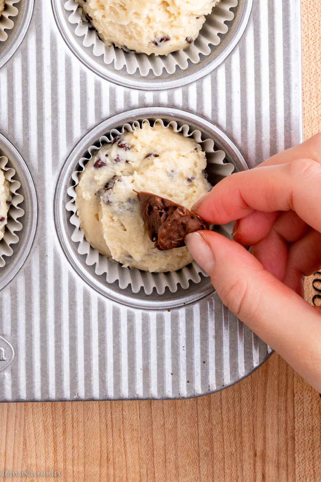 Hand placing nutella in raw muffin batter in metal pan.