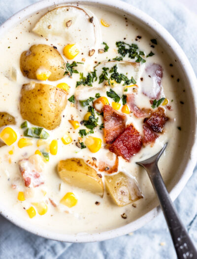 Spoon in bowl of chowder with potatoes and corn