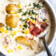 Spoon in bowl of chowder with potatoes and corn