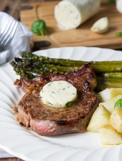 A close a plate with a steak and melting butter with a side of asparagus and potatoes