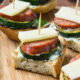 Bread squares with sliced veggies, meat and cheese on top put together with a toothpick.