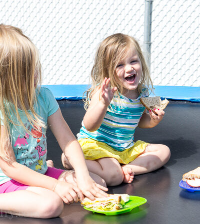 Two little girls eating sandwiches on a trampoline