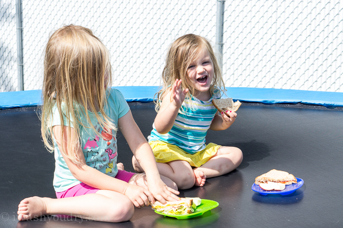 Two little girls eating sandwiches on a trampoline