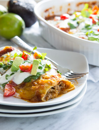 A close up of a food on plate with red sauce and topped with veggies and sour cream