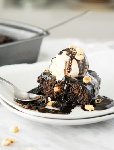 A piece of brownie on a plate, topped with vanilla ice cream, chocolate sauce and nuts