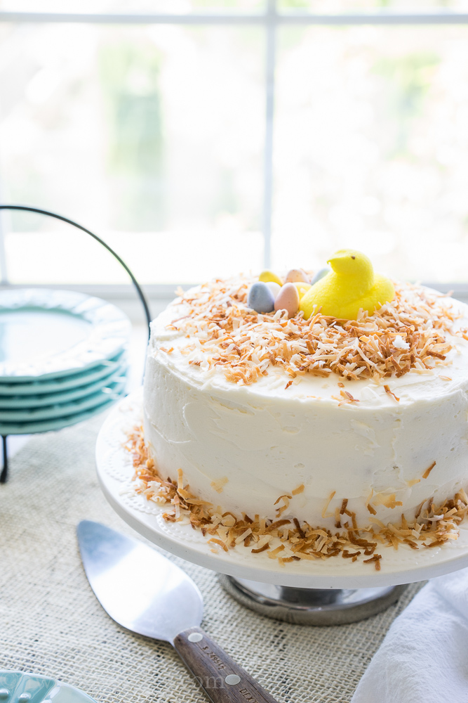 Coconut Cake on white plate, topped with yellow marshmallow peep and toasted coconut.