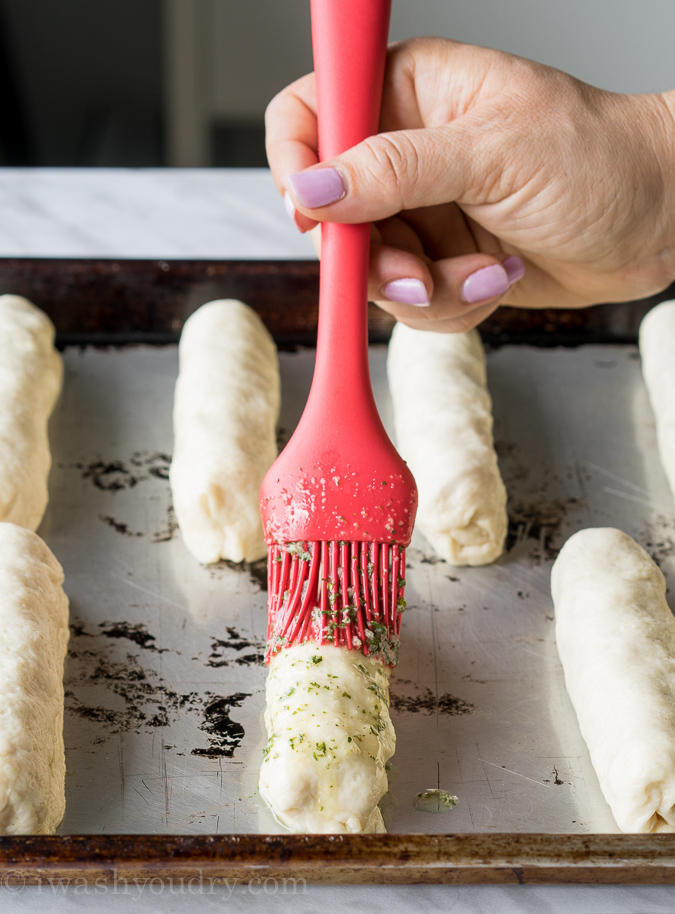 brushing butter mixture over pizza stick on baking sheet.